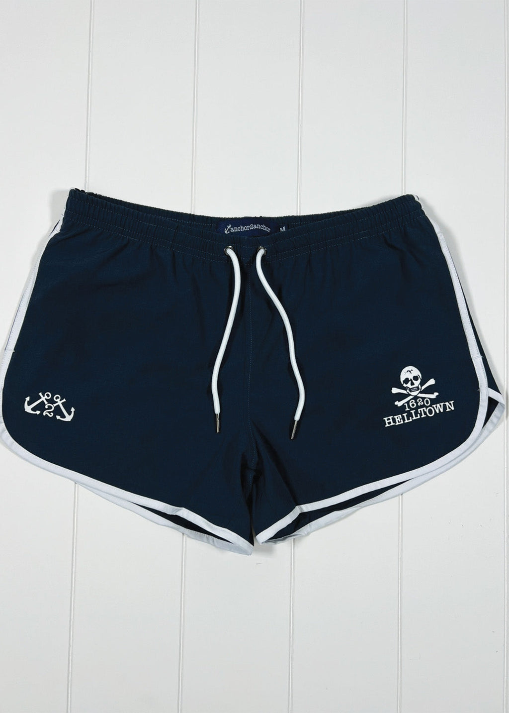 Navy blue shorts with white drawstring and branding on a white wooden background
