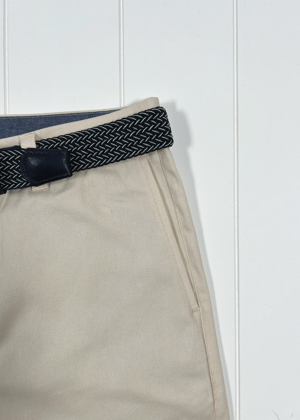 Beige pants with a black and white patterned belt against a white background