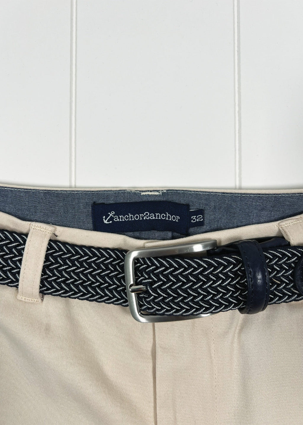 Navy belt with woven pattern and silver buckle on beige pants, brand label visible.