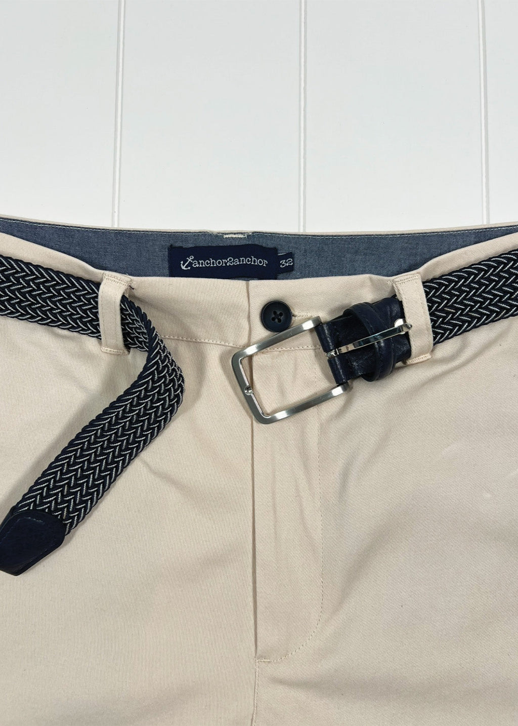 Beige pants with a navy belt featuring a silver buckle on a white background