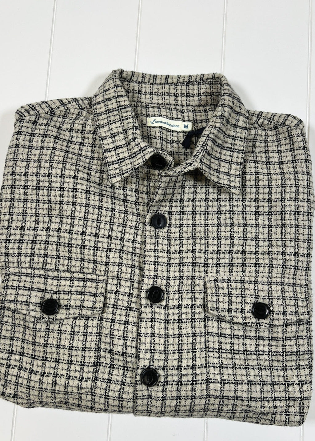 Folded checkered shirt with black buttons on a white wooden surface