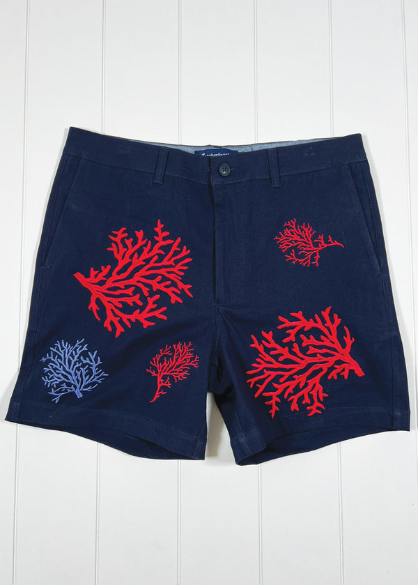 Navy shorts with red and blue coral designs on a white wooden background