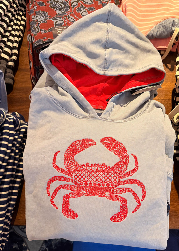 Pale blue hoodie with red crab design on a wooden surface with other clothing items.