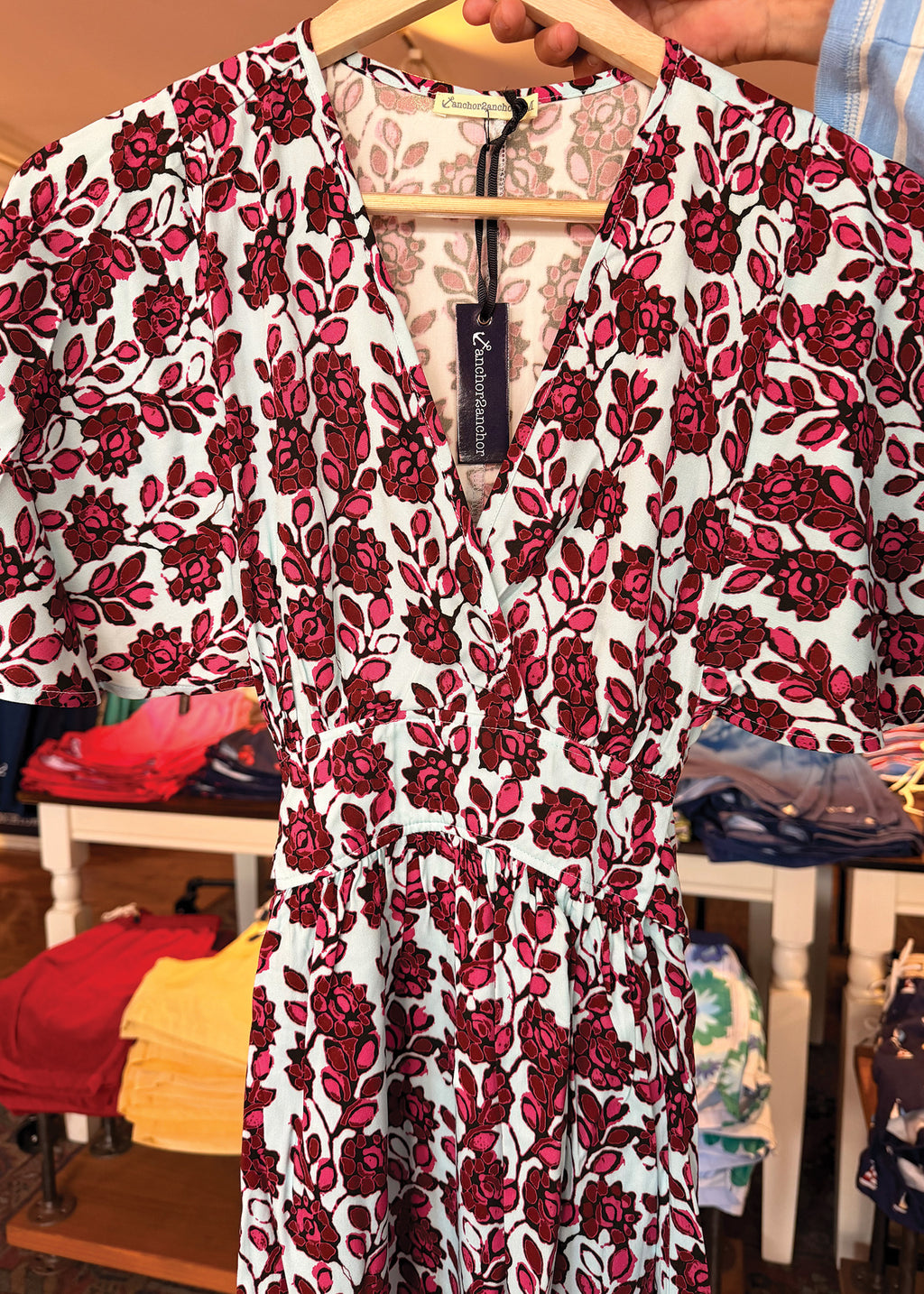 A short-sleeve V-neck dress with a red and dark pink rose floral print on a white background, hanging on a wooden hanger in a retail store.