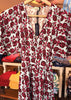 A short-sleeve V-neck dress with a red and dark pink rose floral print on a white background, hanging on a wooden hanger in a retail store.