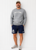 Man wearing a gray 'HELLTOWN' sweatshirt and navy shorts with a skull design, standing against a white wooden panel background.