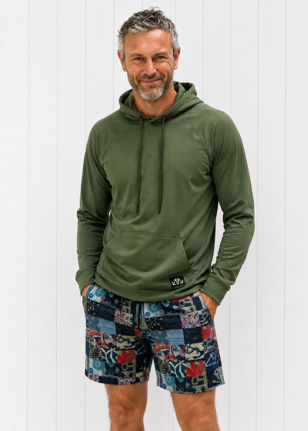 Man wearing a green hoodie and patterned shorts against a white wooden panel background