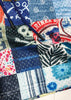 Close-up of a patchwork quilt with various patterns including skulls, flowers, and text.