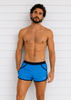 Man wearing blue swim shorts against a white wooden panel background
