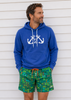 Man wearing a blue hoodie with anchor design and colorful shorts against a white wall.