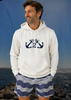 Man wearing a white hoodie with an anchor design and striped shorts standing by a body of water.